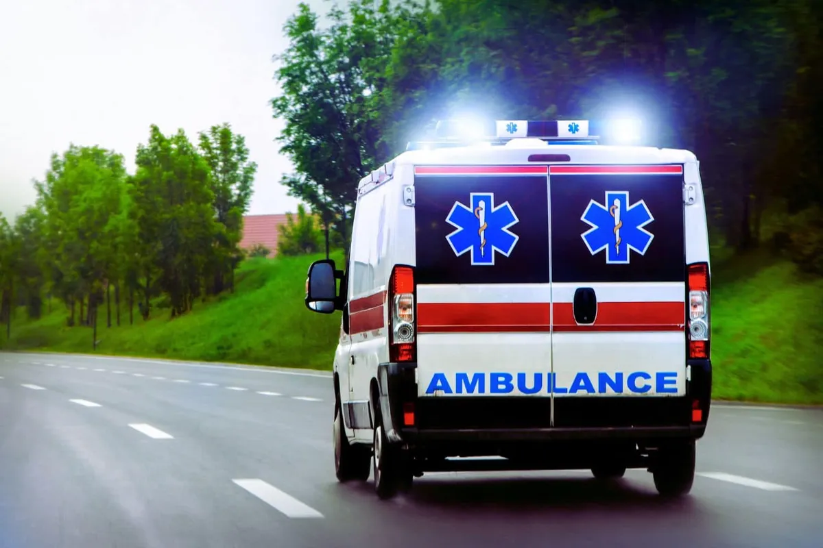 Un taxi ambulancier indépendant en uniforme bleu foncé avec un écusson de la croix rouge sur la poitrine, parcourt une rue animée en ville. Son regard déterminé témoigne de sa formation et de son engagement envers son entreprise.