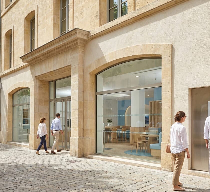 Façade d'une agence bancaire moderne avec des clients marchant sur un trottoir pavé et une personne au distributeur.
