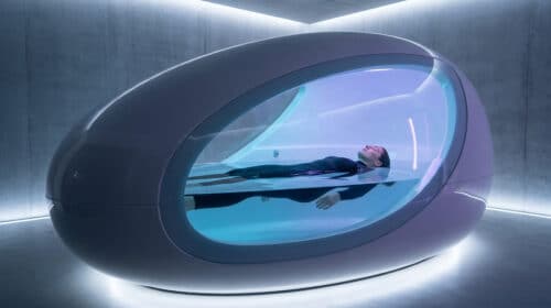 Une femme flotte paisiblement dans un caisson de flottaison futuriste en forme d'œuf au design épuré et lumineux.