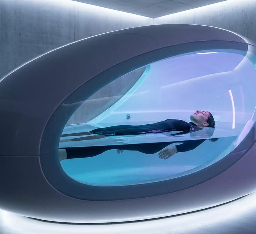 Une femme flotte paisiblement dans un caisson de flottaison futuriste en forme d'œuf au design épuré et lumineux.