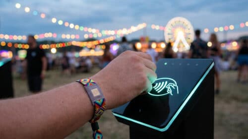 Main utilisant un bracelet électronique pour payer sur une borne sans contact lors d'un festival en soirée.