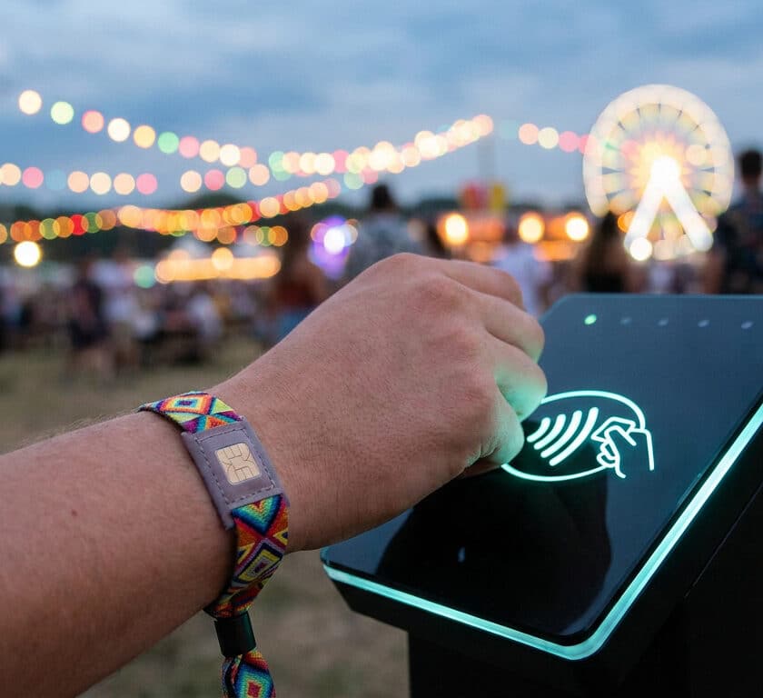 Main utilisant un bracelet électronique pour payer sur une borne sans contact lors d'un festival en soirée.