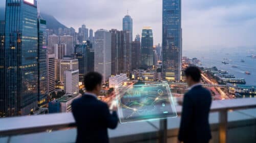 Deux professionnels analysent des données financières sur un écran holographique avec la skyline de Hong Kong en arrière-plan.