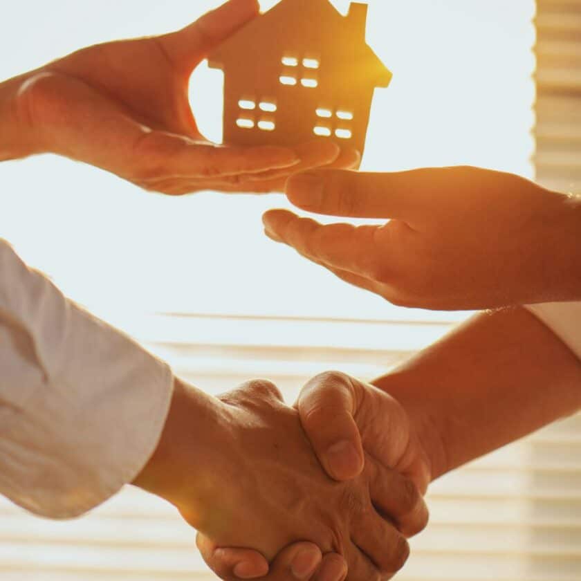 Poignée de main et maison miniature au soleil